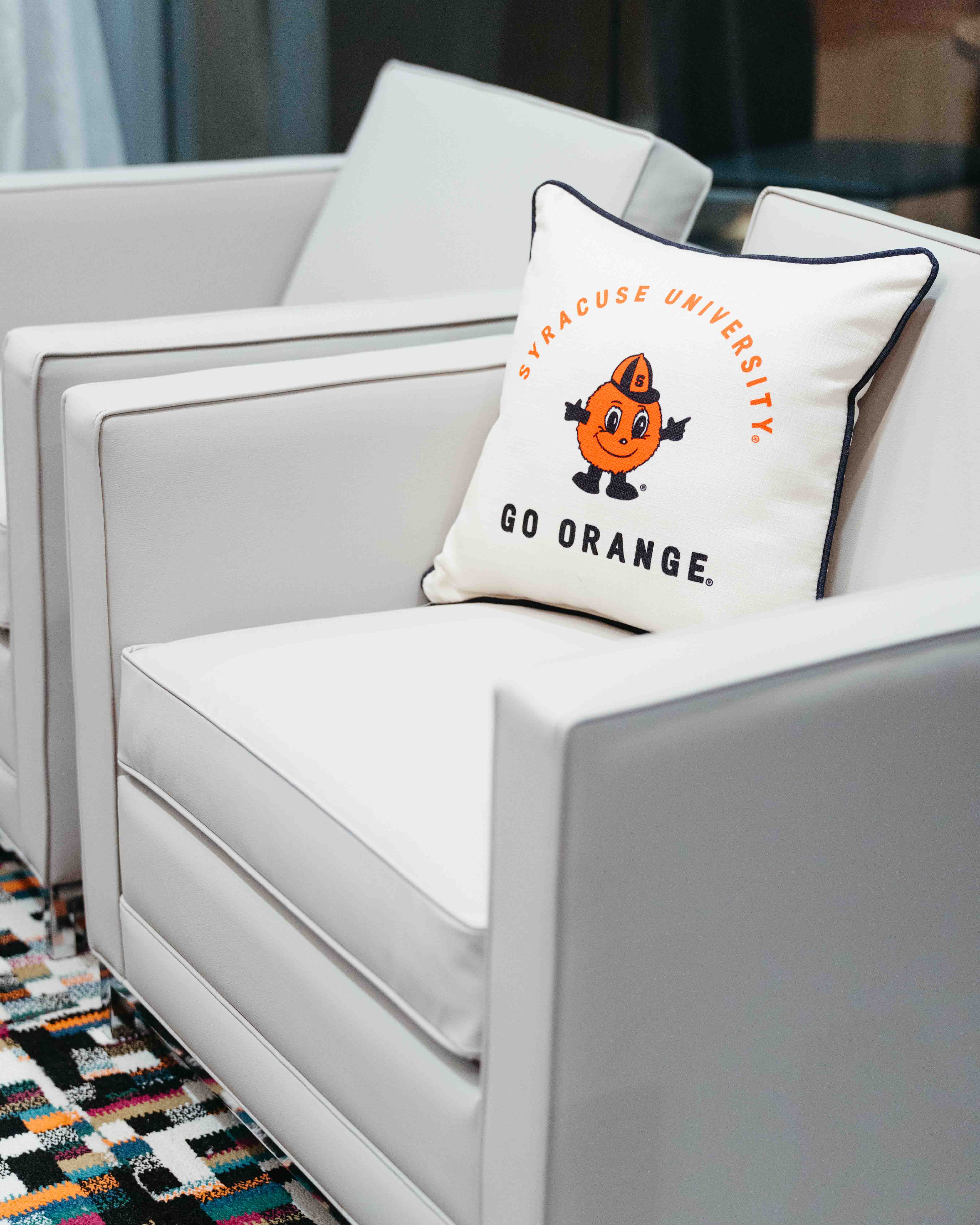 Two white chairs with an Orange Syracuse University "Go Orange" pillow featuring Otto.