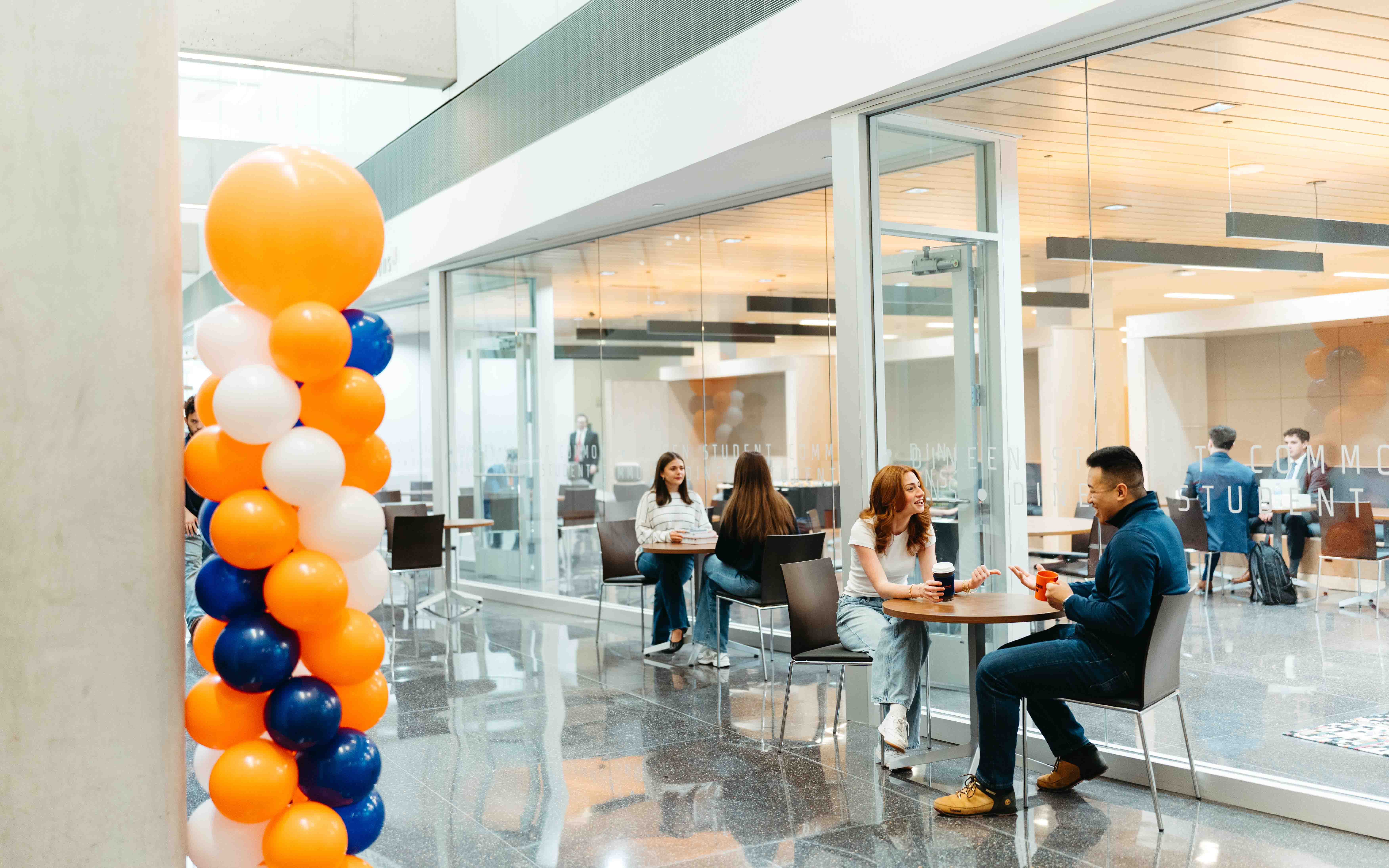 Students sit at tables talking outside of the new Dineen Hall Student Commons