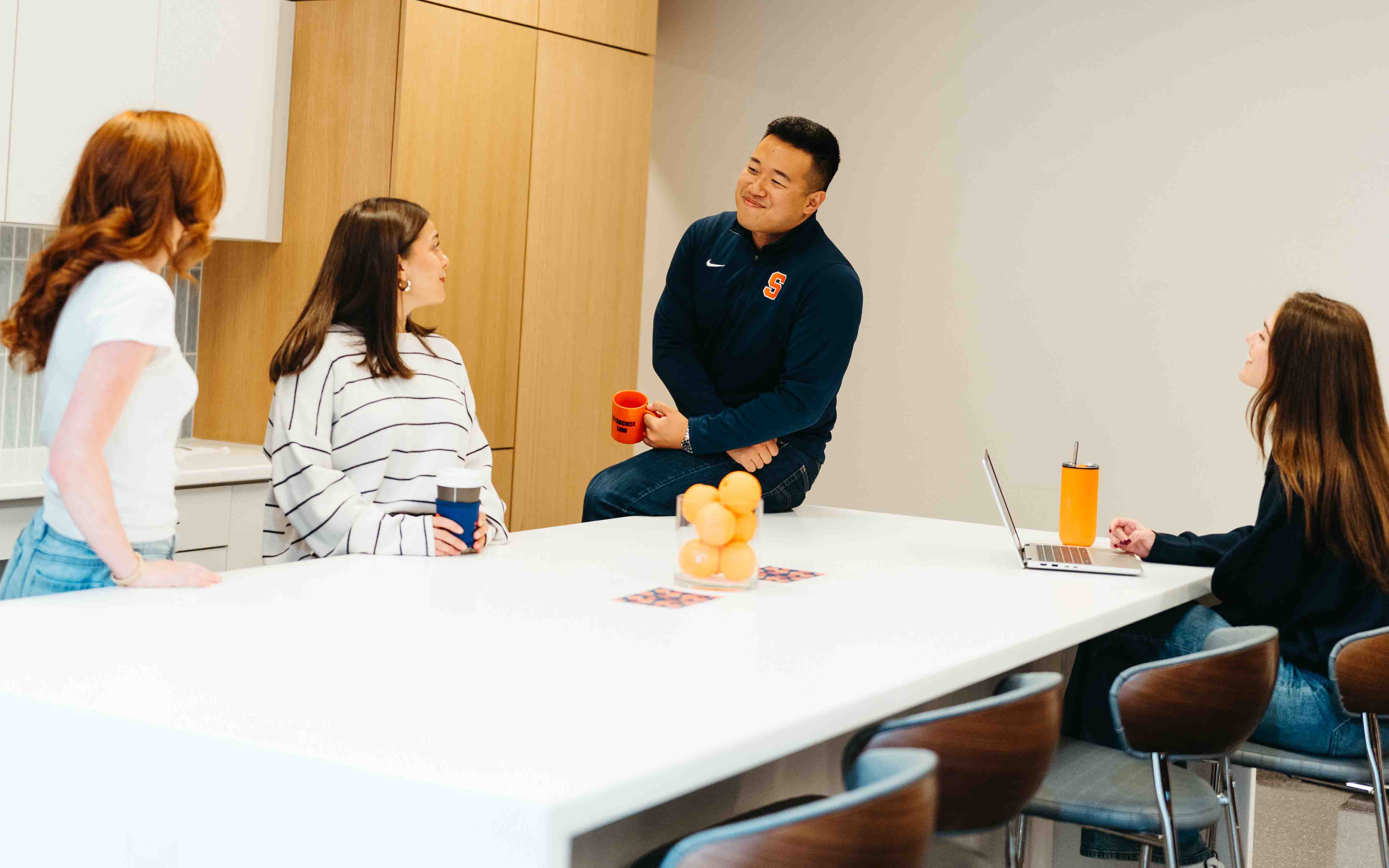 four students gather around the new kitchen with laptops and coffee cups.