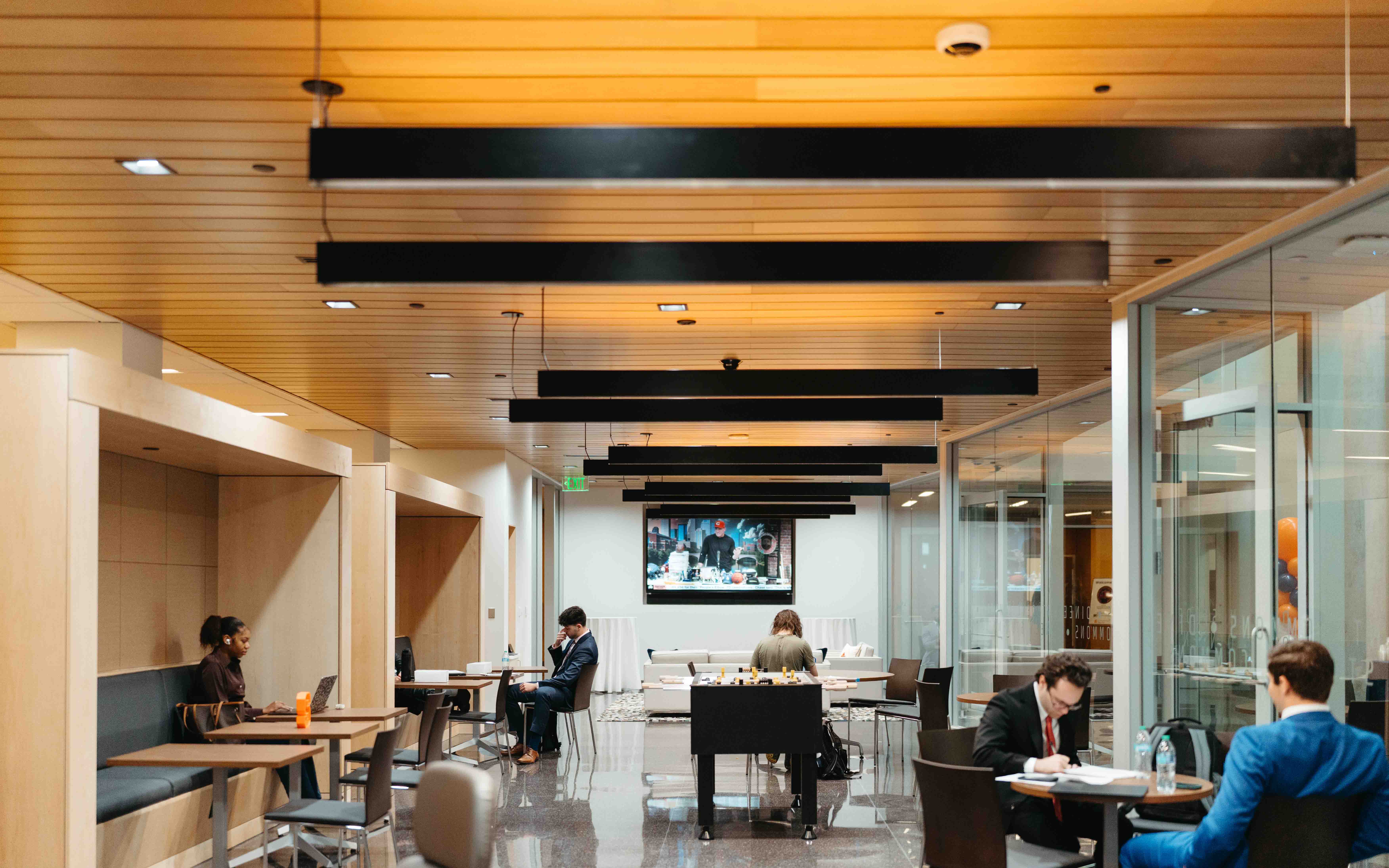 Groups of students enjoy the new student commons space, with a tv on the back wall.