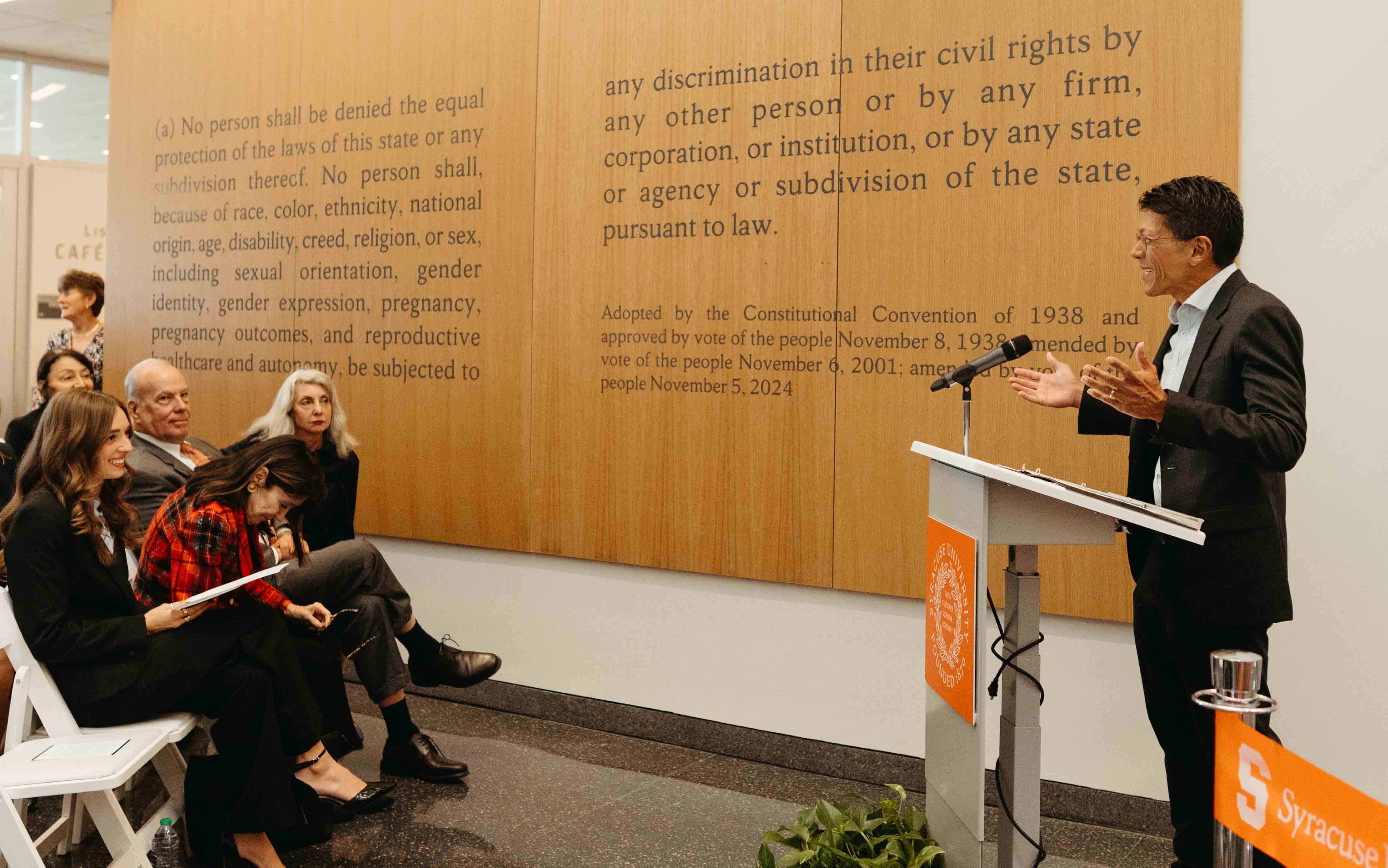 Dean Lau L'98 speaks to guests at the ribbon cutting, who are sitting in chairs in front of his podium.