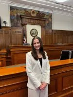 Photo of young woman in white suit with long brown hair in a courtroom