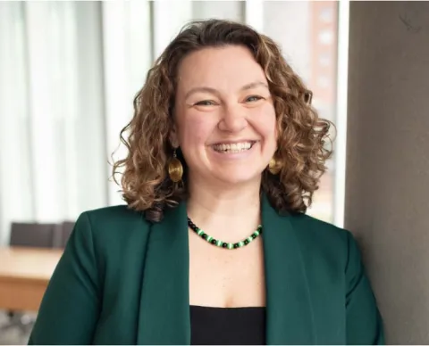 Colleen Gibbons stands in front of a window, wearing a green blazer and a black shirt