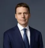 Headshot of man wearing dark suit white shirt blue tie