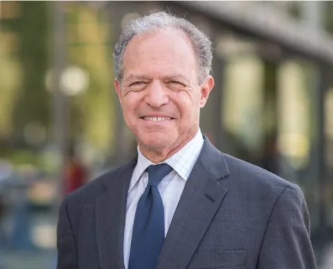 Headshot of Bill Brodsky, standing in front of an out of focus green street scene.