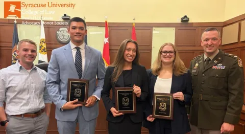 Three men and two women in business attire standing and holding plaques.
