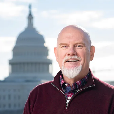 Joe di Scipio smiles in front of the US Capitol building outside in a maroon quarter zip