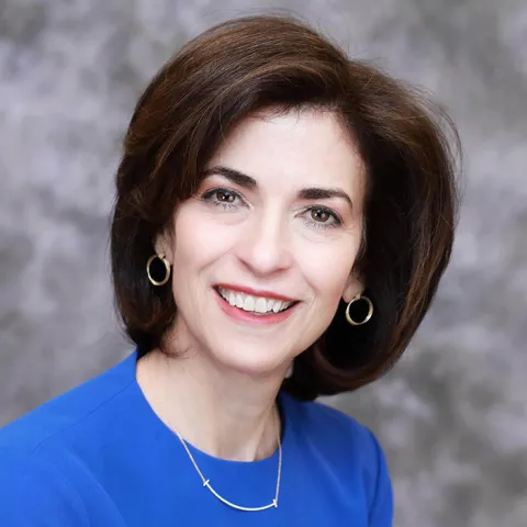 stephanie jacqueney smiling at the camera wearing a blue blouse in front of a marbled gray background
