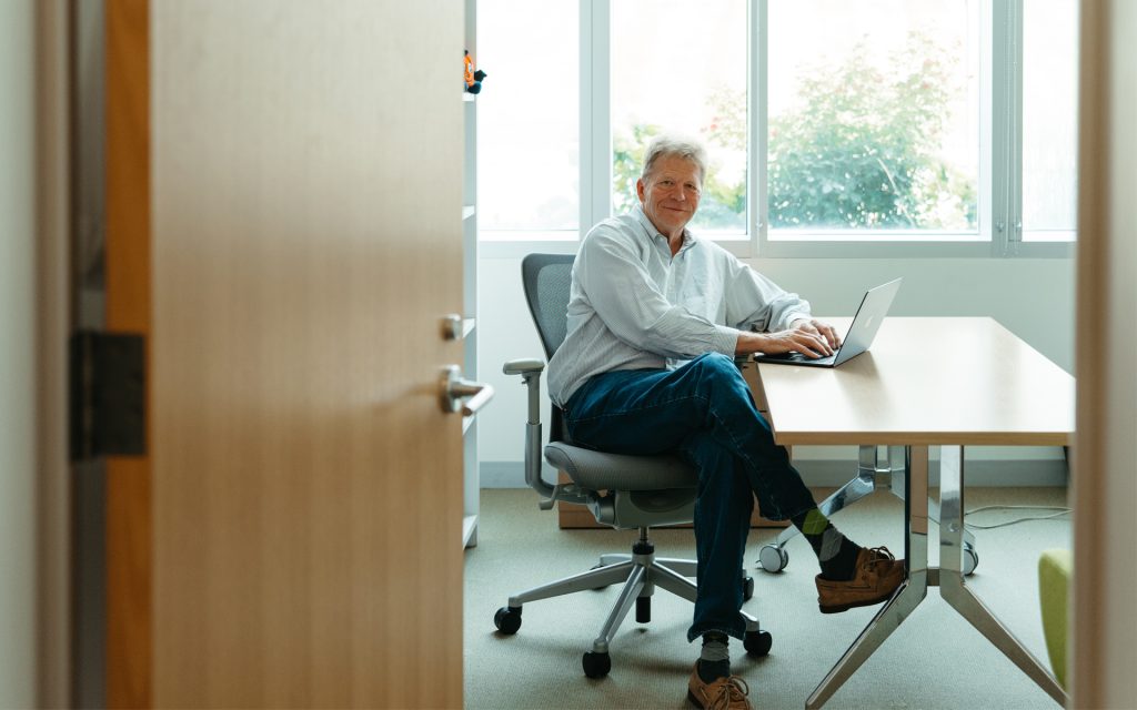 George sits at a desk and looks over through the office