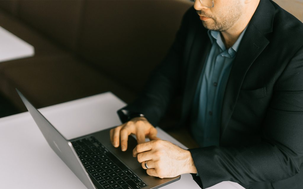 Man sits at desk and types on his laptop computer, wearing a business suit