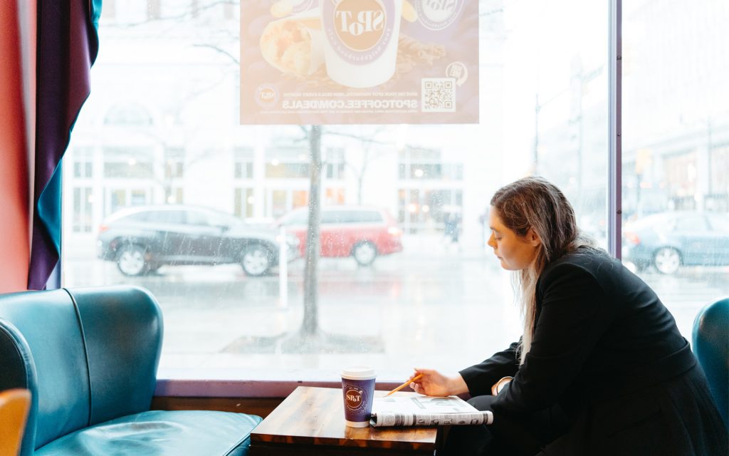 Carly sitting in a coffee shop writing in front of a window