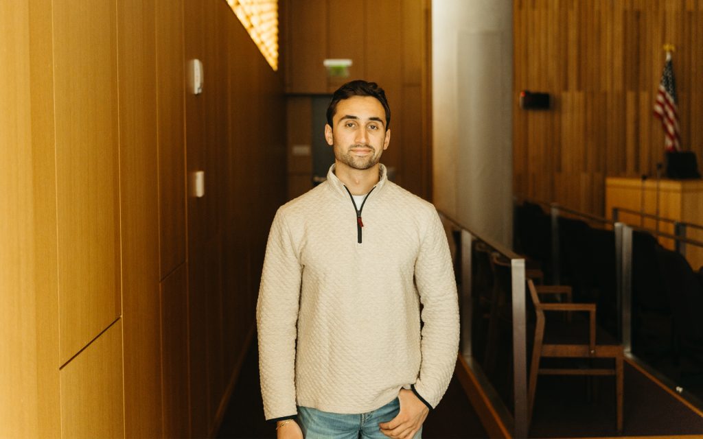 Noah smiles at the camera in a darkened courtroom