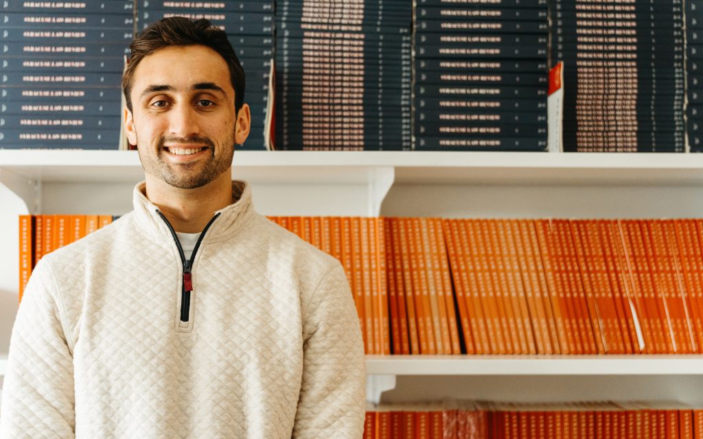 Noah stands in front of a blue and orange stack of Law Review publications on a shelf