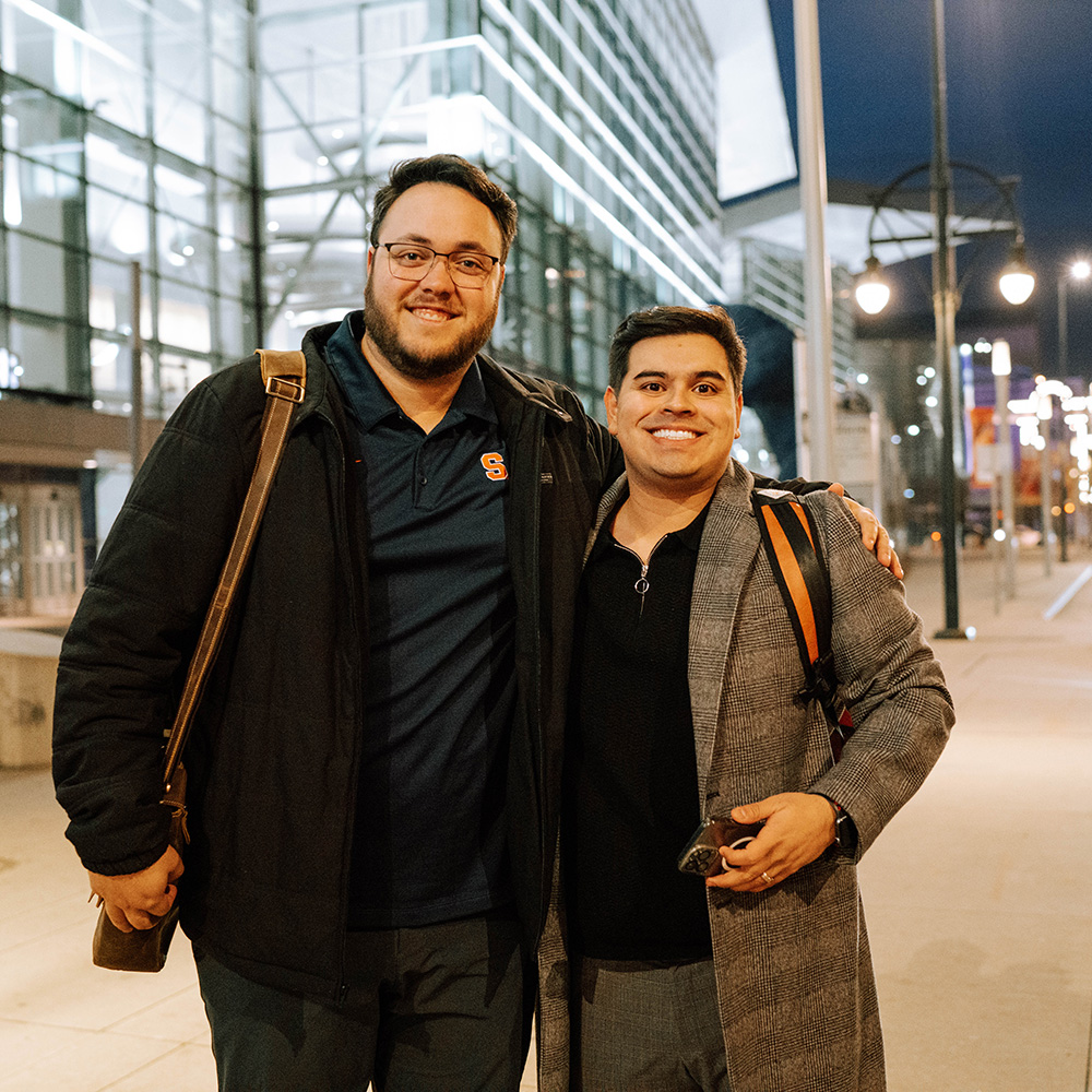 two students stand with their arms around each other smiling at the camera