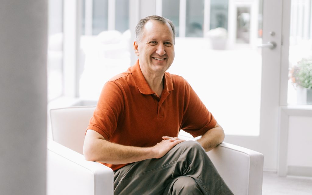 John Dougall sits in a chair in Dineen Hall and smiles for the camera.