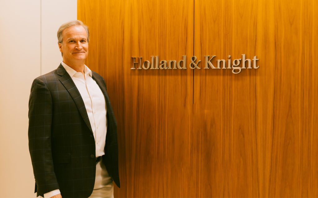 Richard Furey L&rsquo;94 poses next to the Holland &amp; Knight sign