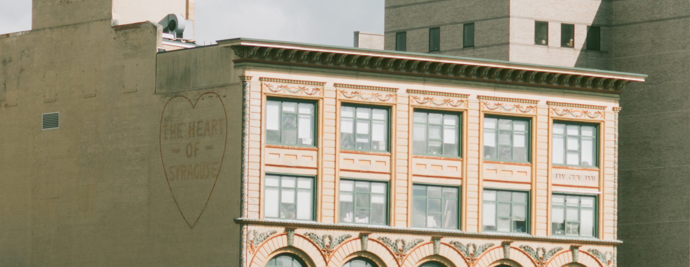 Image of a high rise building with a mural on the side that says "the heart of Syracuse"