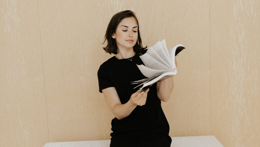 Kaitlin Sommer leafs through a book and looks at the pages, wearing a black dress