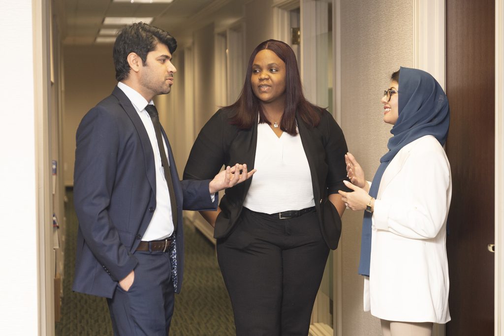 three LL.M. students congregate in a hallway, looking at each other and talking.