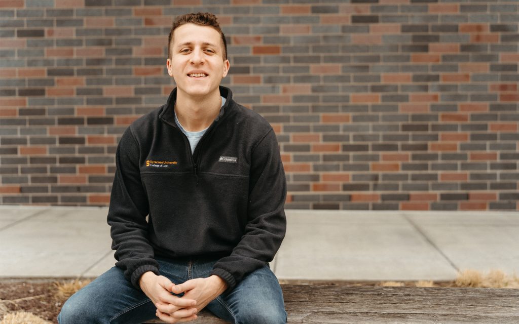 Zach Mazuzan site in front of Dineen Hall outside on a bench smiling