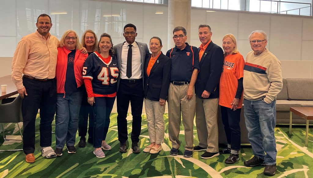 Adam Katz stands with a group of 10 people in the atrium smiling with the winner of the Mordue Scholarship