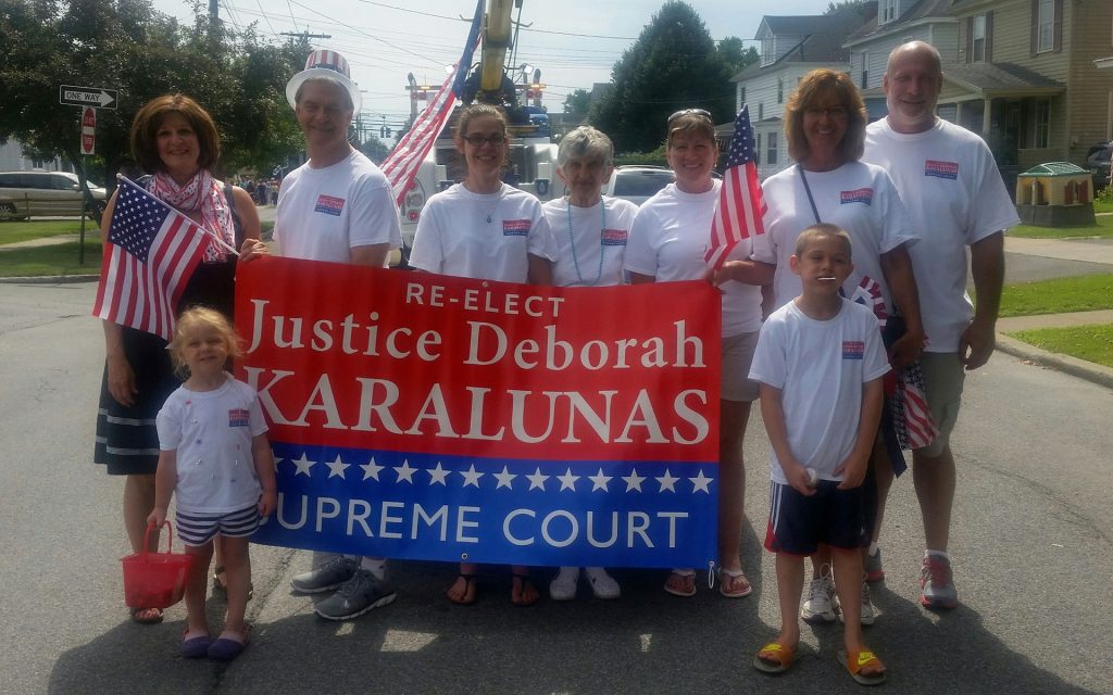 Judge Karalunas and her family hold up a sign saying Re-elect Justice Deborah Karalunas to the Supreme Court