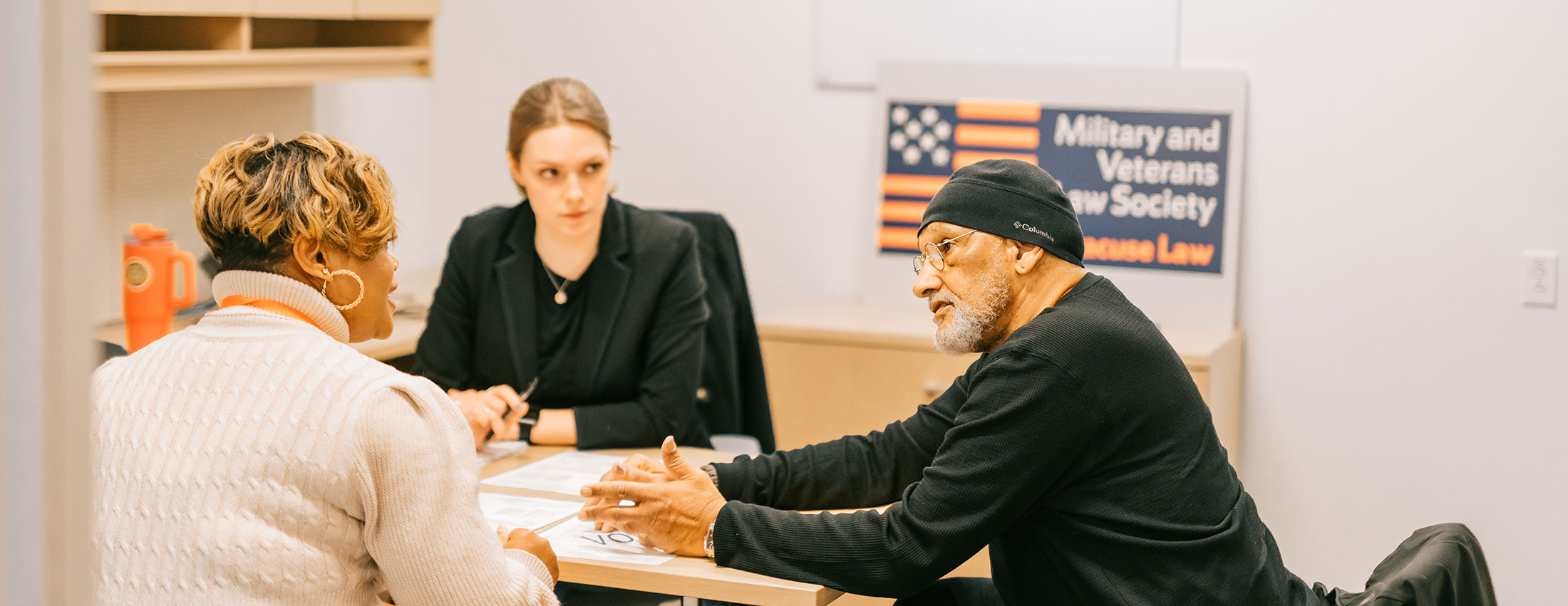 three people meet around a desk in an office for the military and veterans legal aid society
