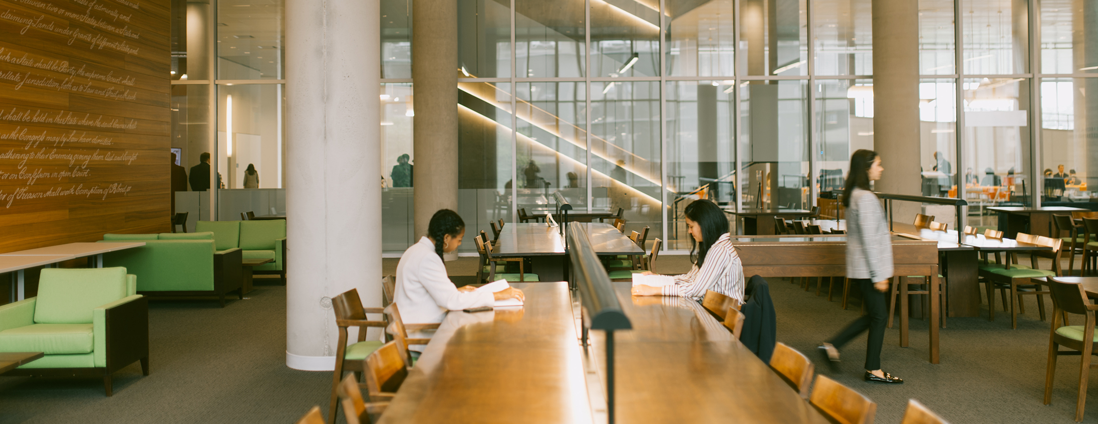 two students at a desk in the syracuse law library studying, and a third walking to the right