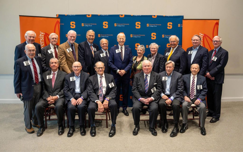 17 members of the Class of 1968 gather for a group photo in front of the Syracuse University step-and-repeat.