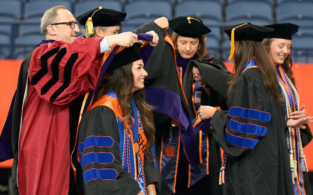 Todd Berger places a commencement hood on graduating student Emery Bielecki.