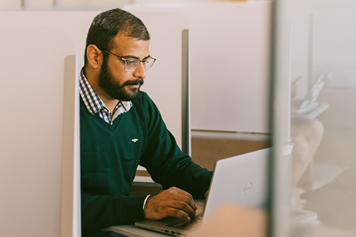 A man working on a laptop at a desk in an office setting.