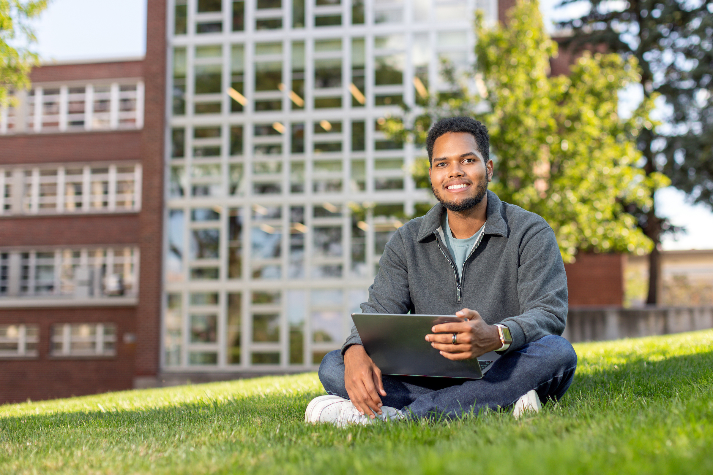 Luis Perez sitting outside in the grass with his computer at Syracuse University's campus. 
