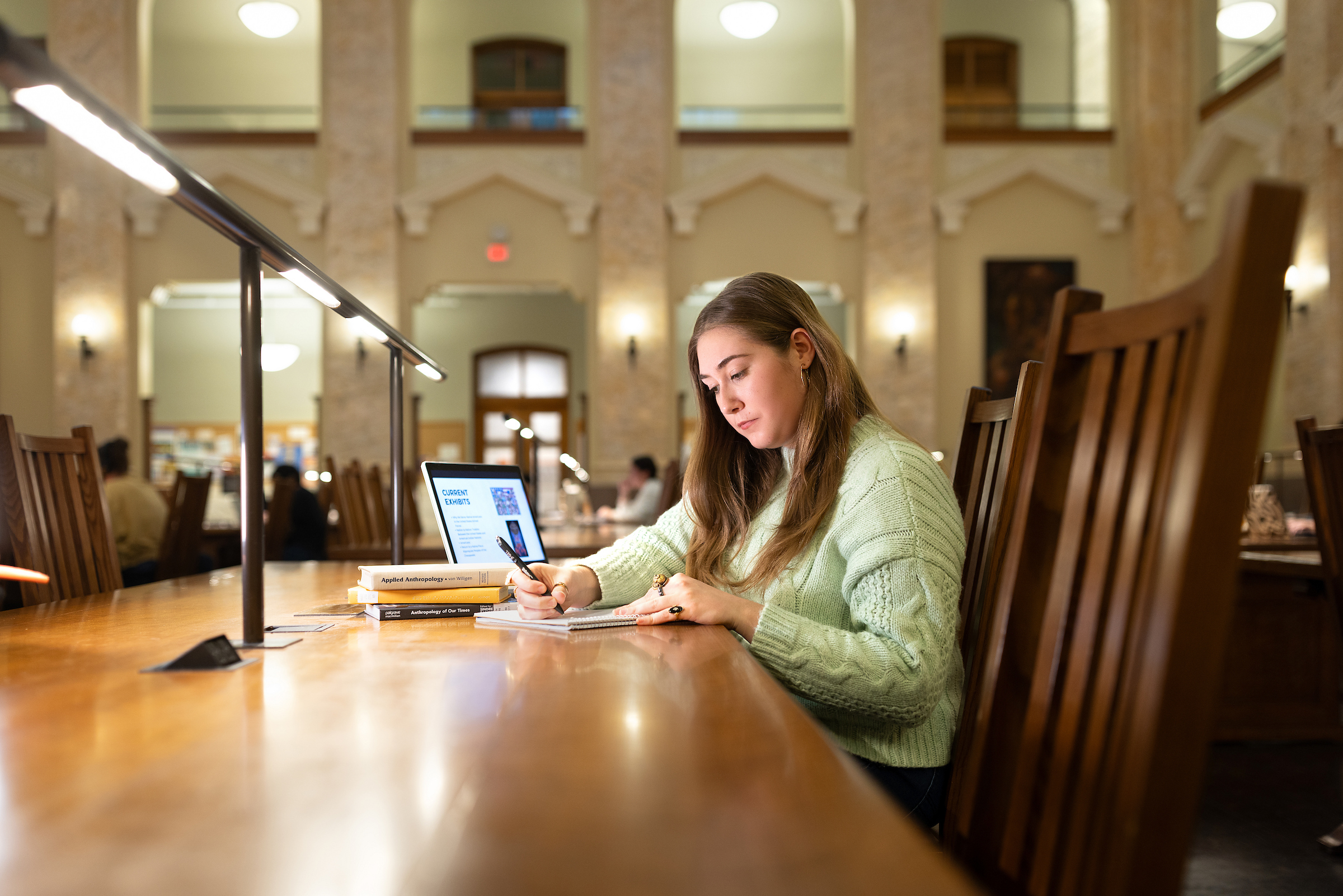 Taylor Bryne sitting in a library on a computer and taking notes in a notebook. 