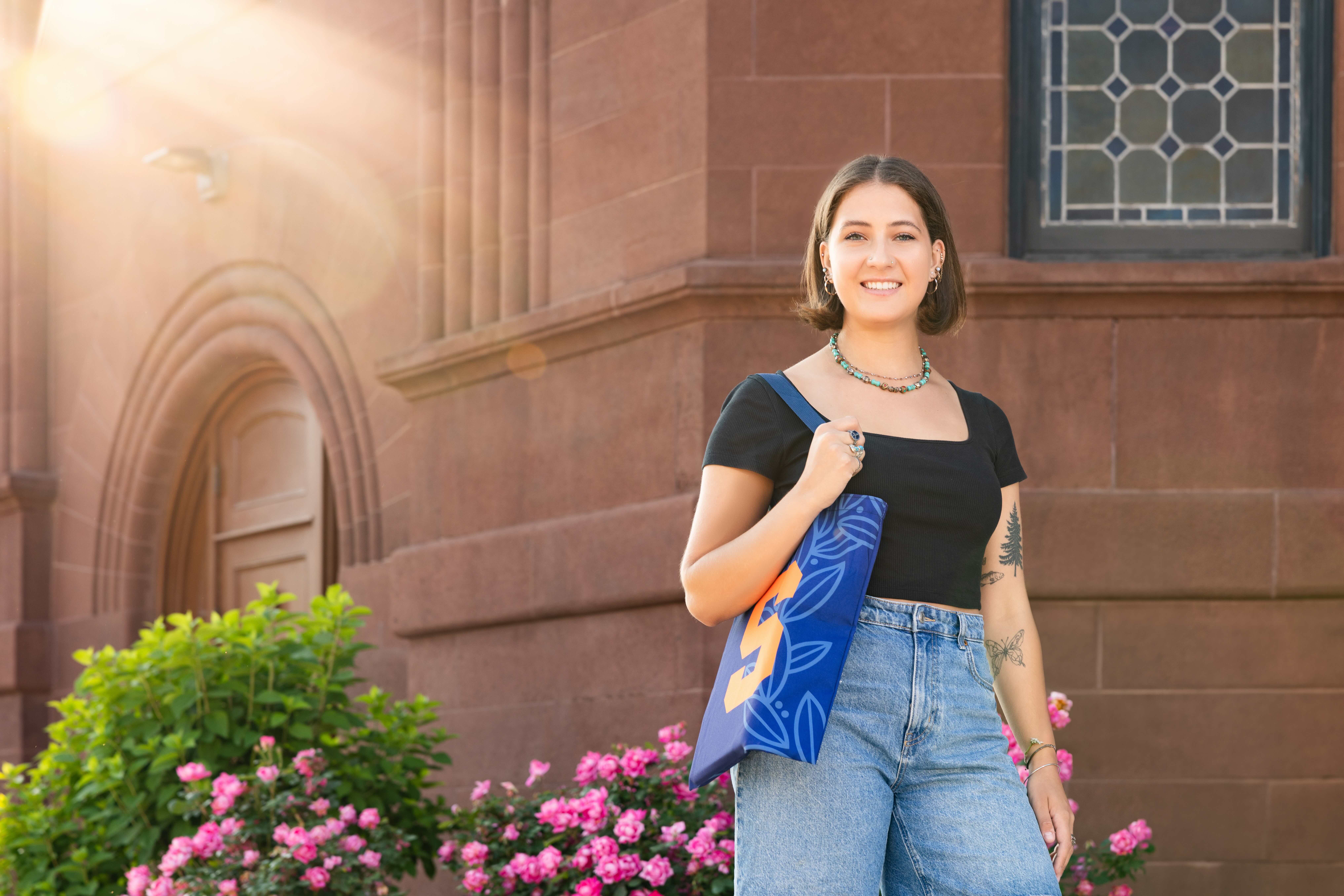 A student stands outside on campus holding a bag. 