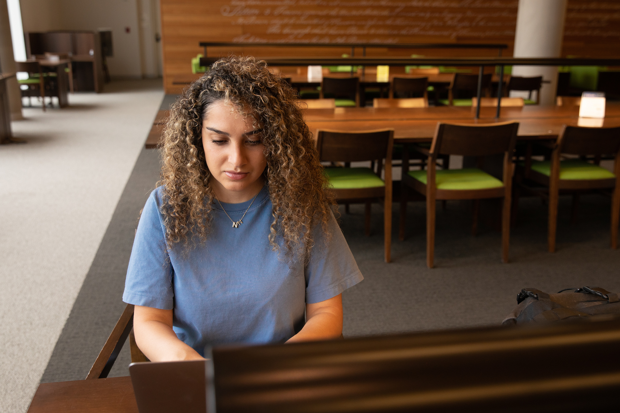 A student sitting inside a library working independently on their computer. 